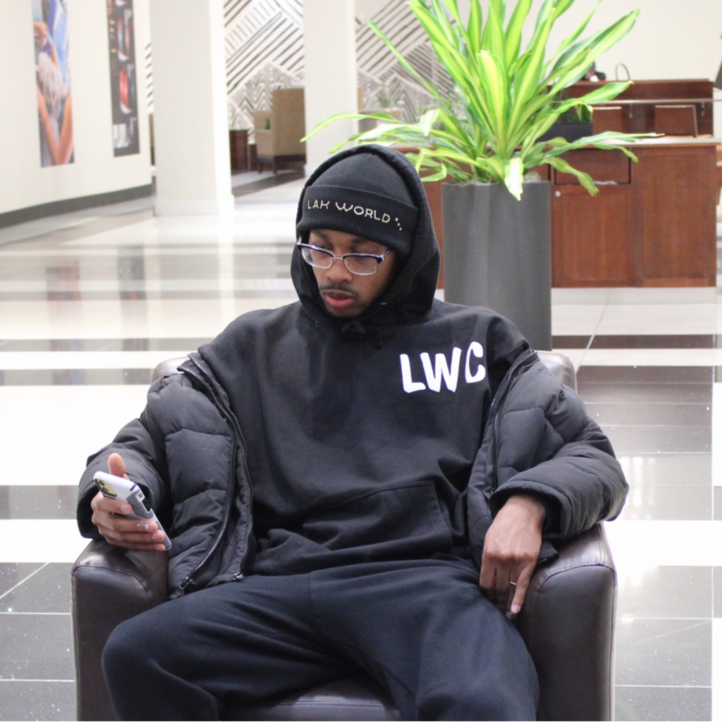 A person sitting in a chair wearing a black hooded sweatshirt with the text 'LWC' on the front, paired with black pants.